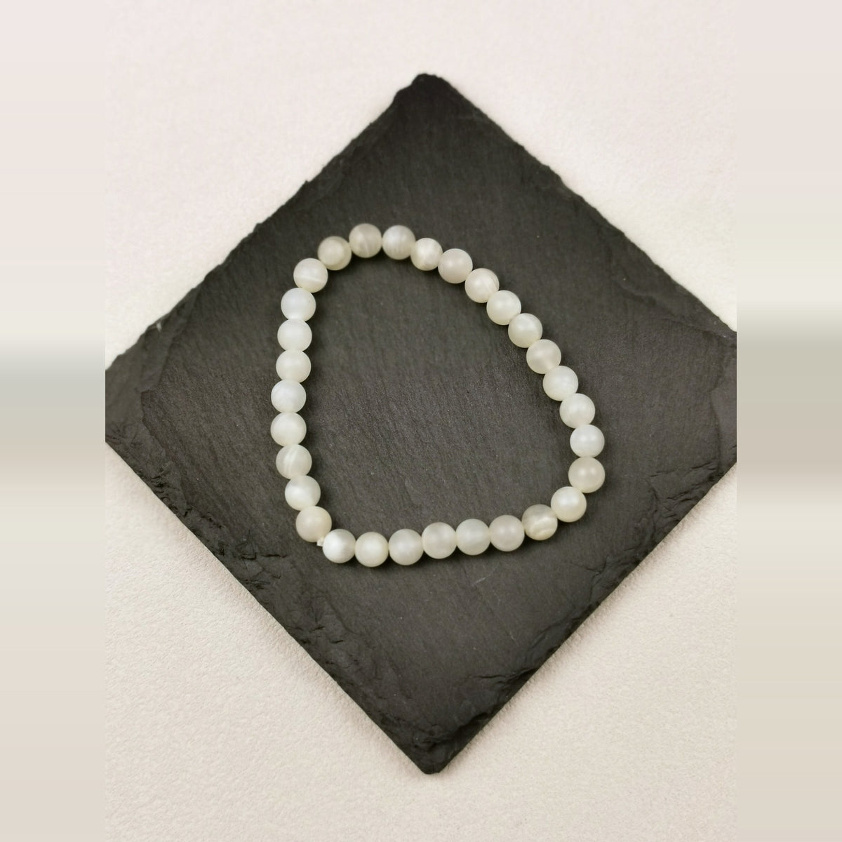 Armband aus runden cremeweißen Mondsteinperlen mit 6 mm auf Schieferplatte