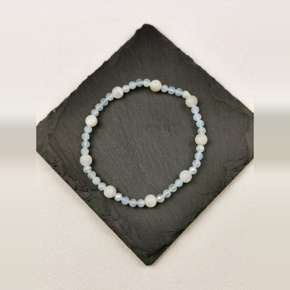 Armband aus facettiertem Aquamarin mit weißen Mondsteinkugeln auf Schieferplatte