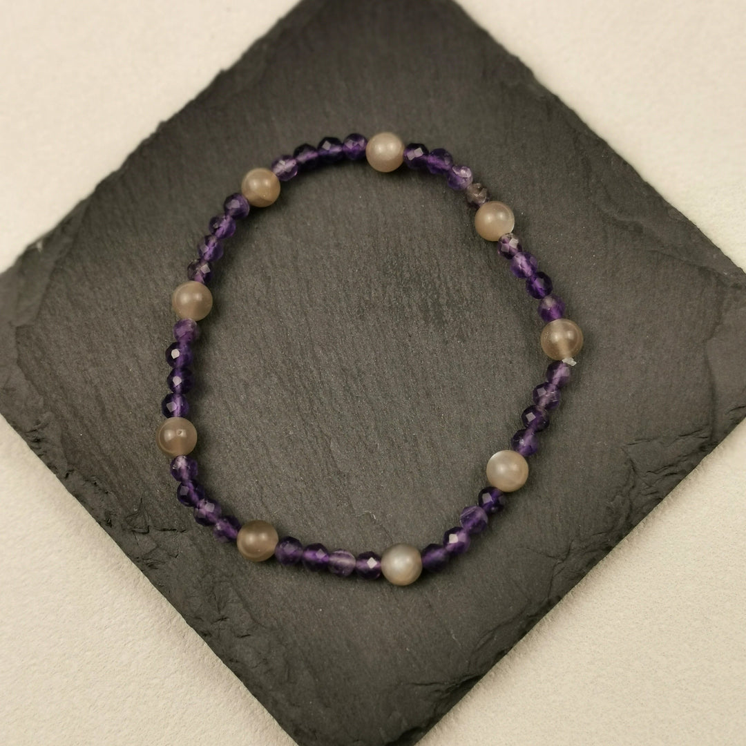 Armband aus facettiertem Amethyst mit grauen Mondsteinkugeln auf Schieferplatte