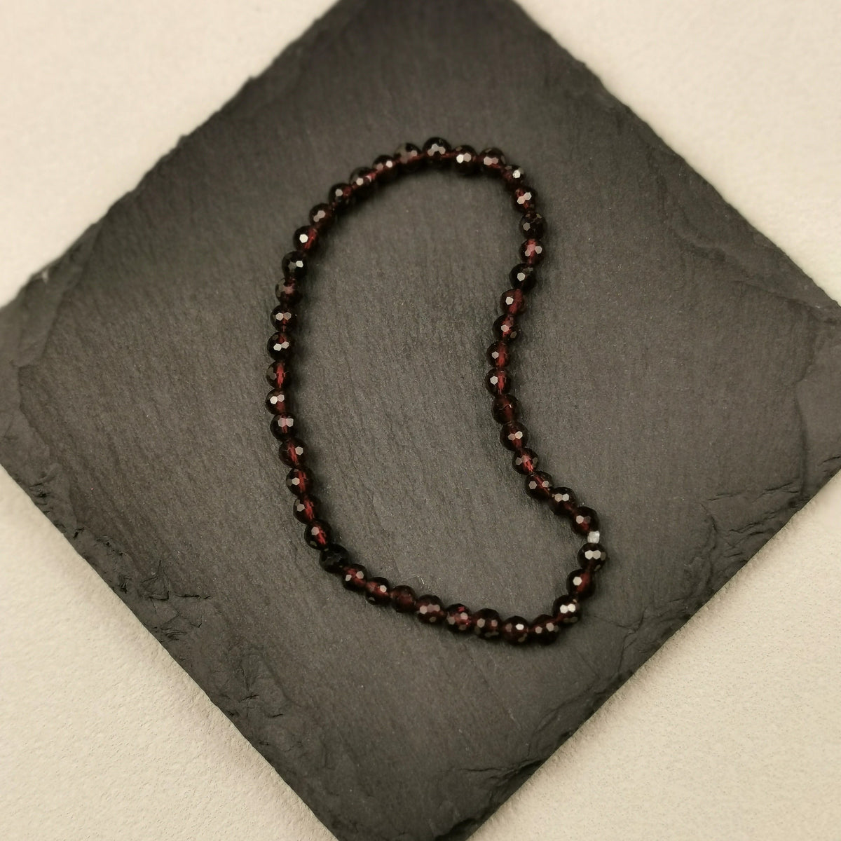 Armband aus facettierten dunkelroten Granatperlen mit 4 mm auf Schieferplatte